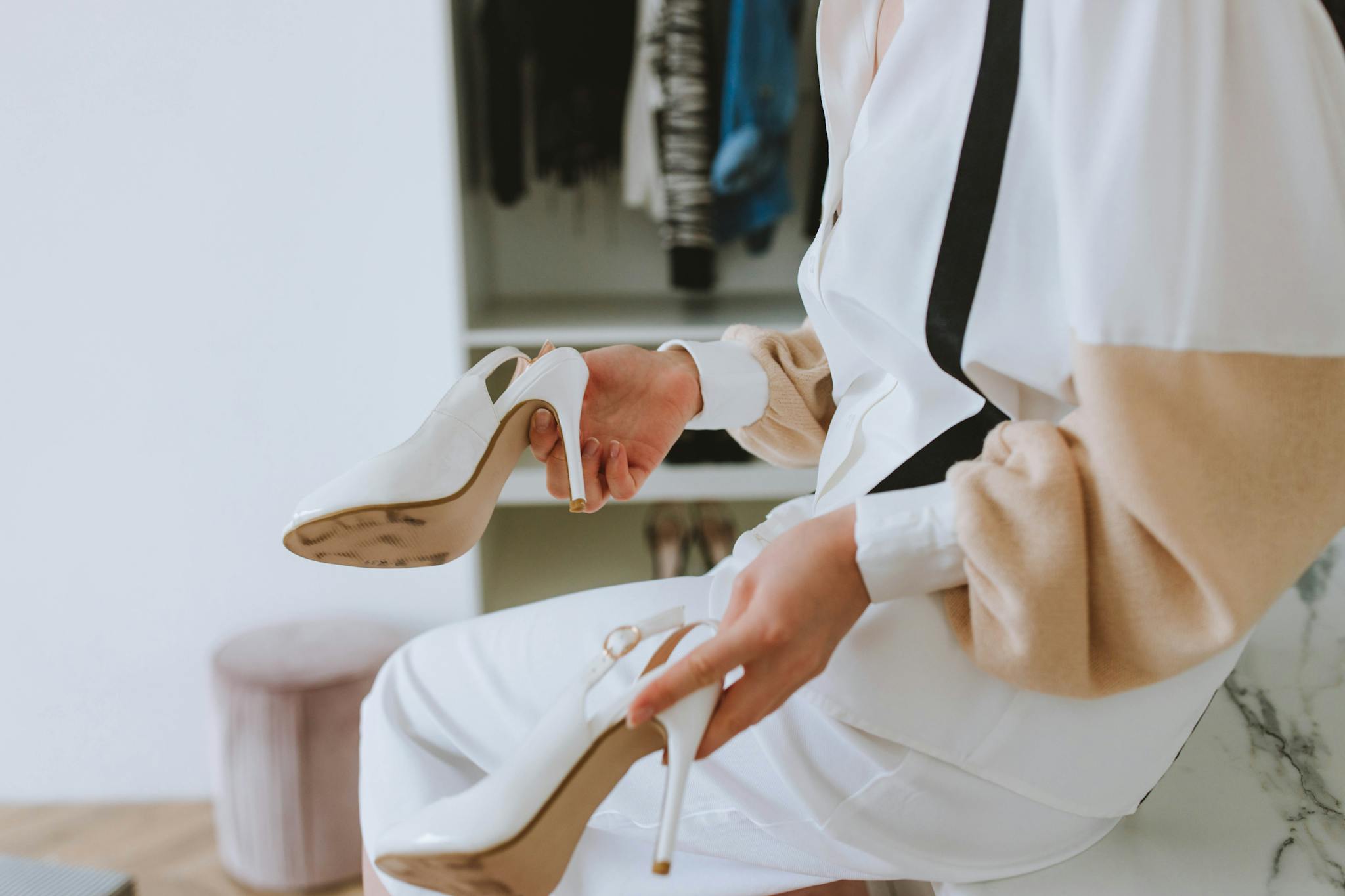 Elegant woman trying on chic white heels in a stylish closet.