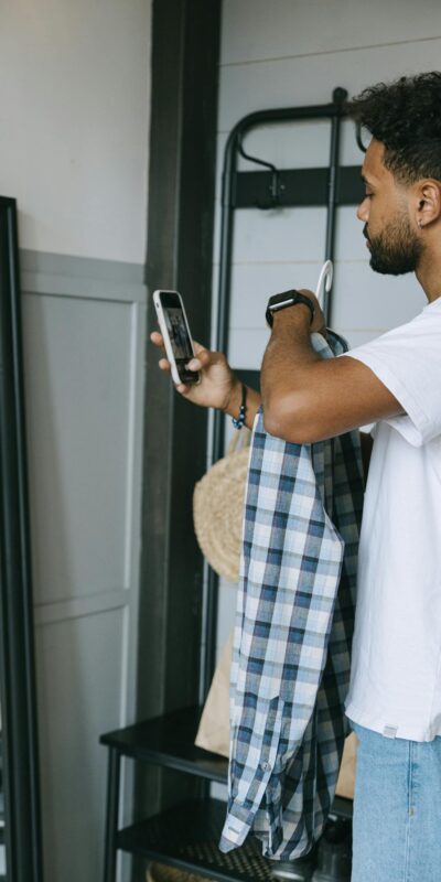 Young man holding a plaid shirt and using smartphone for online shopping. Casual indoor setting.